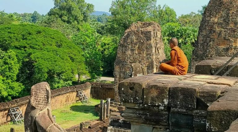 Jeune moine bouddhiste en robe orange méditant au sommet d'un temple au Cambodge.