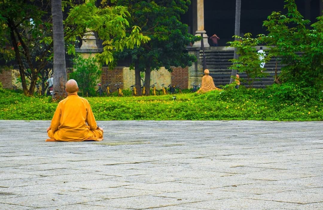 Moine bouddhiste en méditation dans la nature, enveloppé de brume, avec en arrière-plan une grande statue translucide du Bouddha symbolisant la paix intérieure.