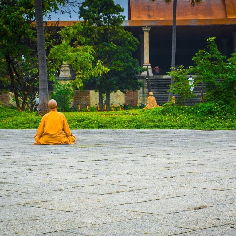 Moine bouddhiste en méditation dans la nature, enveloppé de brume, avec en arrière-plan une grande statue translucide du Bouddha symbolisant la paix intérieure.